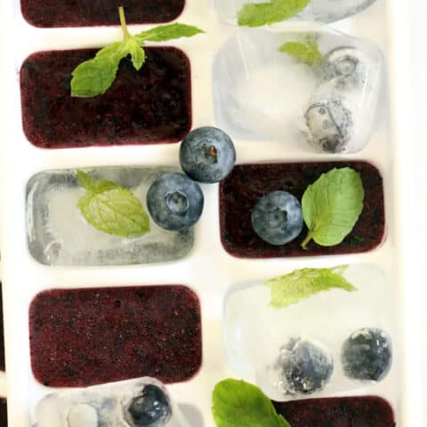 A white ice cube tray filled with blueberry ice cubes.