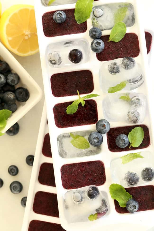 Two white ice cube trays filled with blueberry ice cubes.