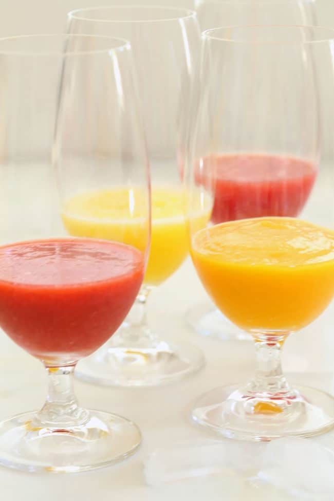 Four clear drinking glasses filled with fresh fruit agua frescas.