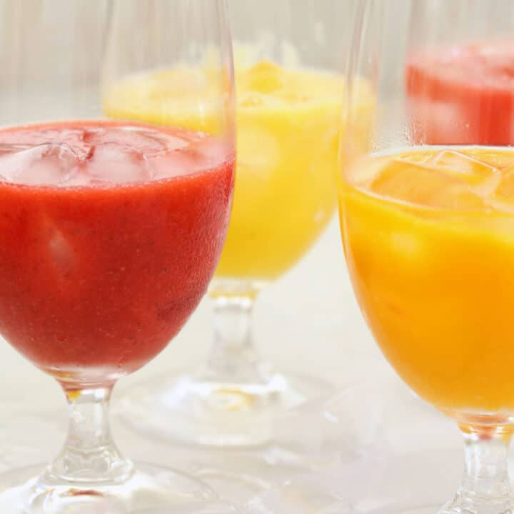Four clear drinking glasses filled with fresh fruit agua frescas.