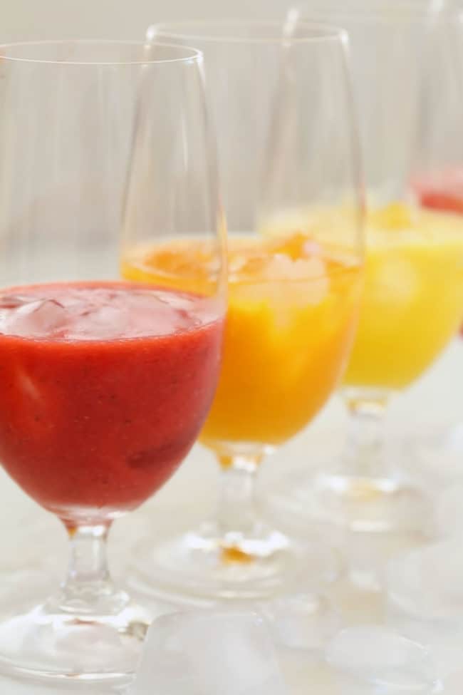 Four clear drinking glasses filled with agua frescas and ice.