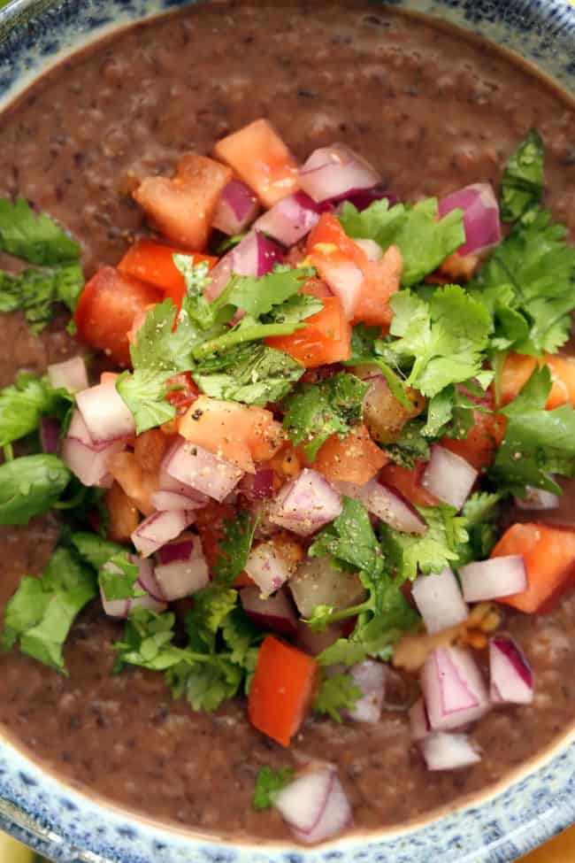 A white and blue bowl filled with black bean dip garnished with pico de gallo.