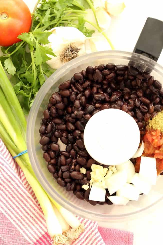 A food processor filled with beans, salsa, chopped onion, garlic and spices.
