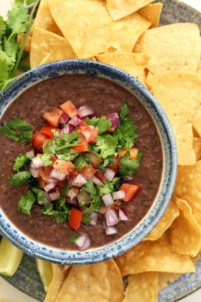 A bowl of black bean dip with tortilla chips on a plate next to it.