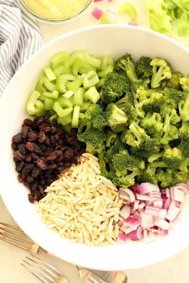 A white bowl filled with raisins, chopped celery, slivered almonds and chopped onions.