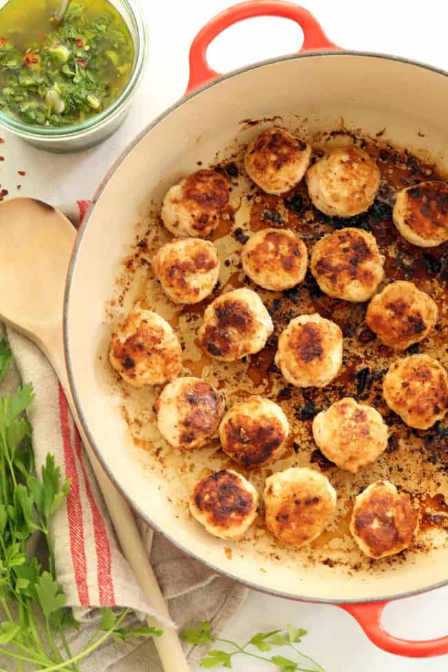 A red Dutch oven filled with browned ground meat. A wooden spoon rests next to the pot.