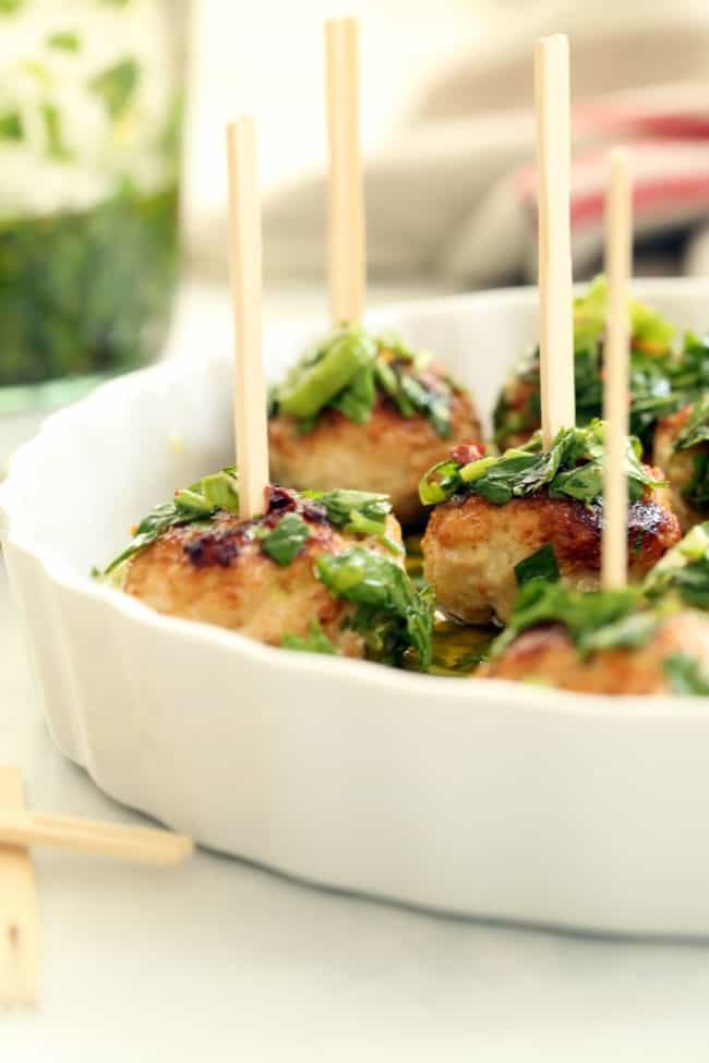 A white tray filled with Chicken Chimichurri Cocktail Meatballs with wooden skewers poked in them.