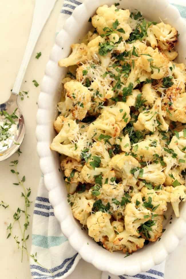 A white serving dish filled with roasted cauliflower pieces topped with grated parmesan cheese.