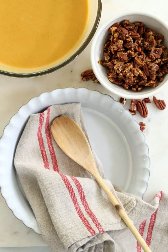 A white pie dish with a dish towel and wooden spoon resting in it.