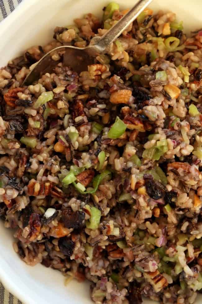 A white bowl filled with wild rice salad A spoon rests in the bowl.