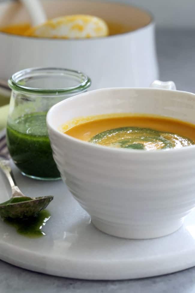 A white cup filled with pureed vegetable puree. A small glass jar filled with pesto sits next to the cup.