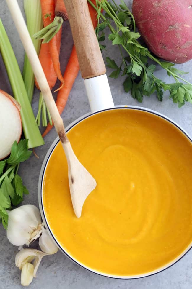 A white pot filled with pureed vegetable soup. A wooden spoon rests in the pot.