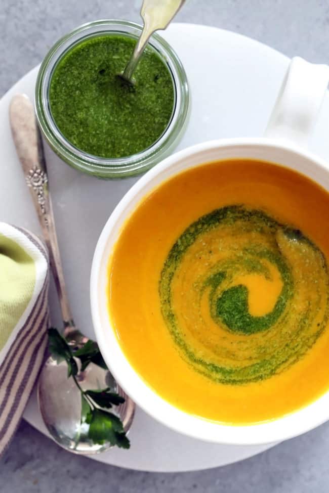 A white bowl filled with French Potage Soup. A small glass jar filled with pesto sits next to the bowl.