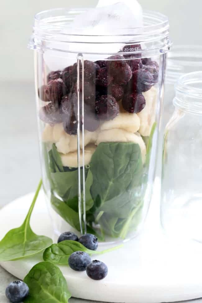 A blender container filled with fruit and spinach.