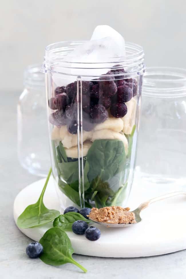 A clear blender filled with fruit, berries and greens. 