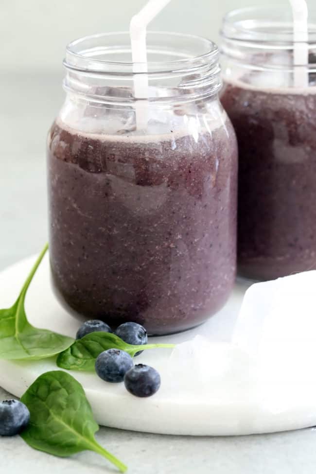 Two clear mason jars filled with blueberry spinach smoothie.