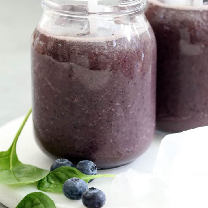 Two clear glasses filled with blueberry spinach smoothie