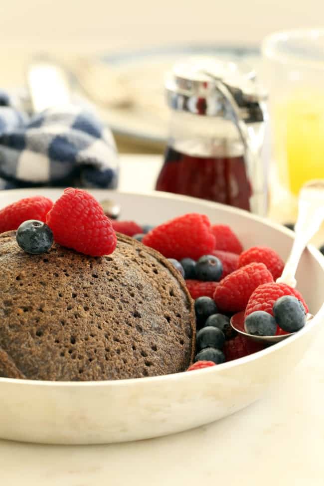 A platter filled with flapjacks and fruit. A spoon rests in the fruit.