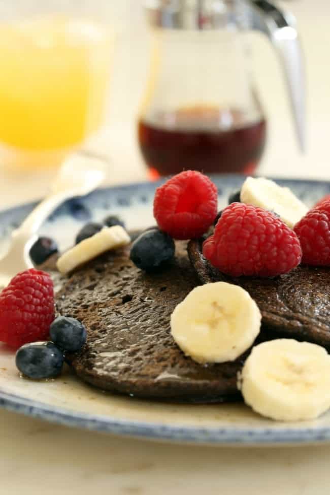 A blue and white plate filled with buckwheat pancakes and fruit.
