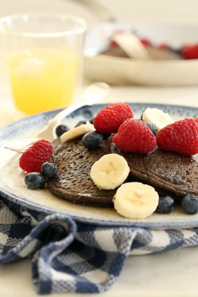 A blue and white plate filled with buckwheat pancakes topped with fruit.