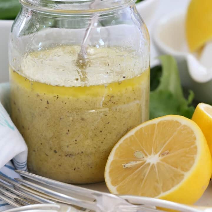 glass mason jar half filled with lemon mustard vinaigrette. A blue and white napkin and half a lemon sits next to the jar.