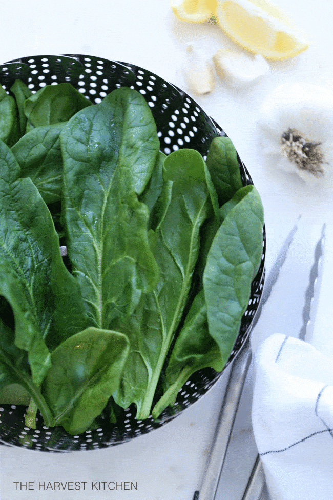A steamer basket filled with fresh spinach leaves.
