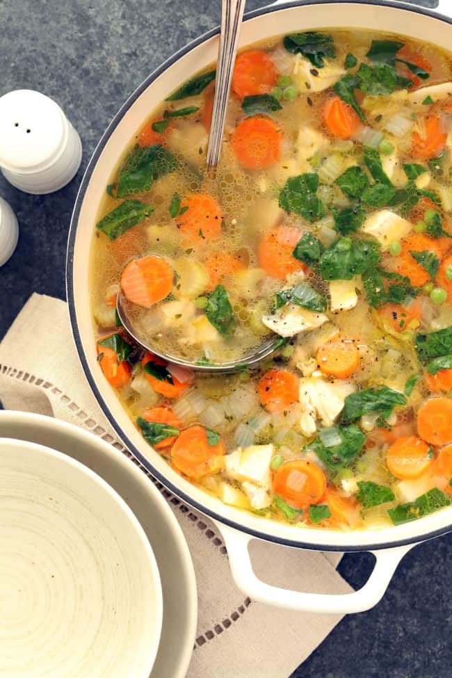 A white pot filled with spring chicken vegetable soup.