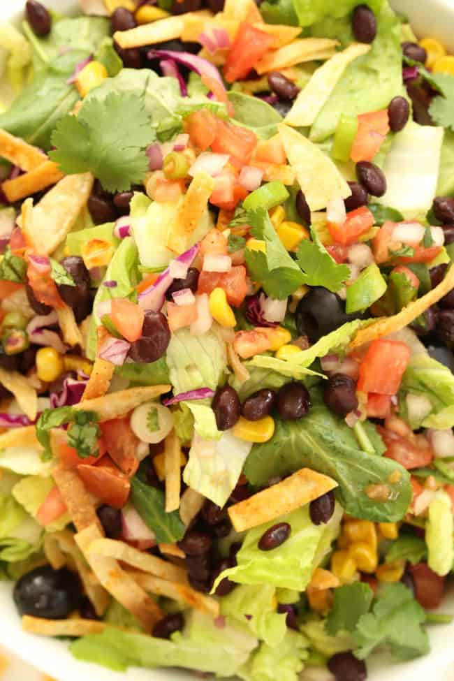 white bowl filled with tossed lettuce, beans, tomatoes and tortilla chips.