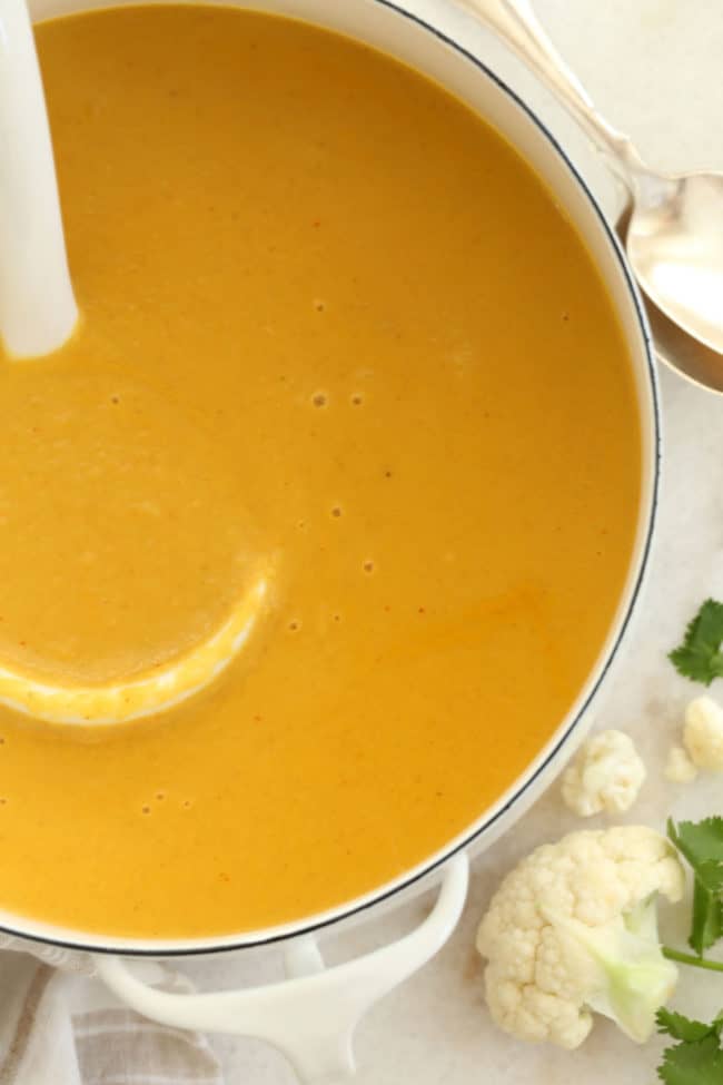 A white pot filled with coconut curried cauliflower soup. A white ladle rests in the pot.