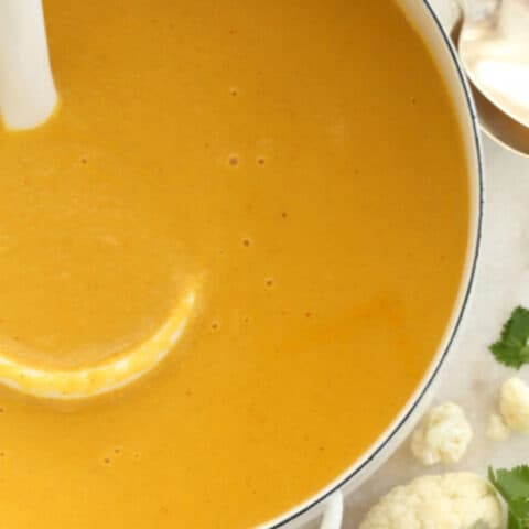 A white pot filled with Roasted Coconut Curry Cauliflower Soup. A white ladle rests in the pot.