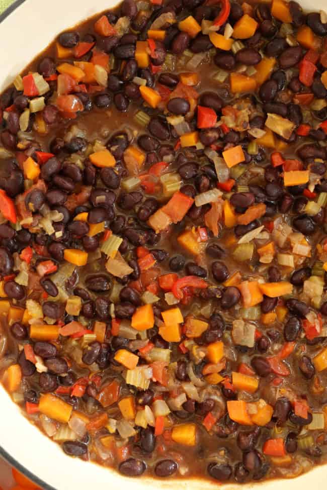 A white pot filled with legumes and vegetables.