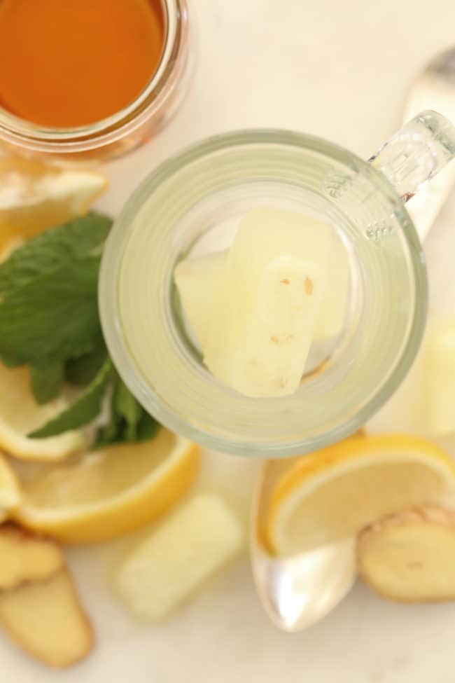 A clear glass cup sits next to several lemon wedges and a container of honey.