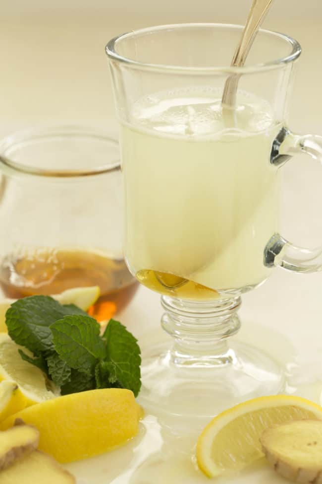 A clear glass cup with ginger ice cubes in water with honey.