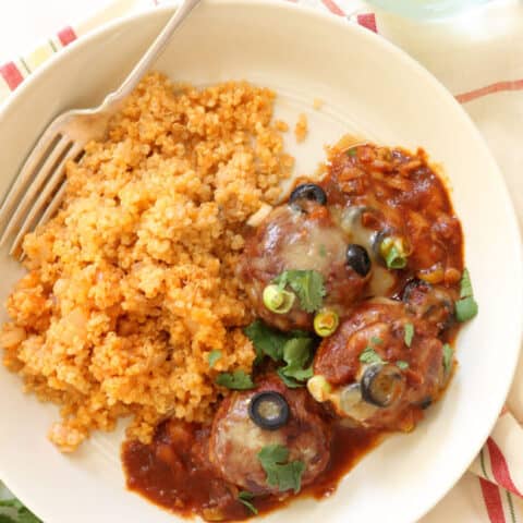 A white plate with Mexican meatballs in enchilada sauce and Spanish rice.