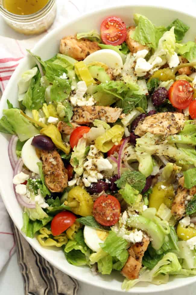 White bowl filled with green salad and grilled chicken for Greek salad recipe