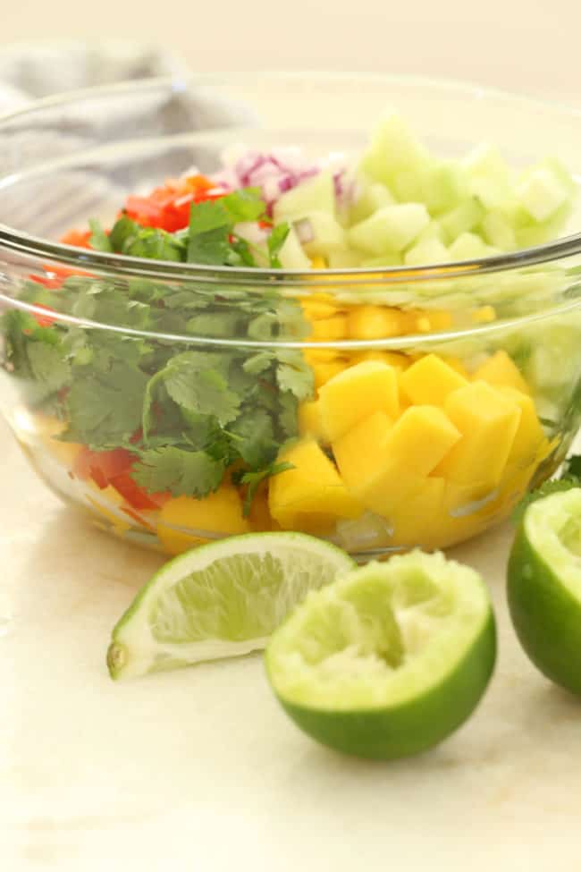 A clear glass mixing bowl filled with mango salsa (salsa de mango) ingredients.