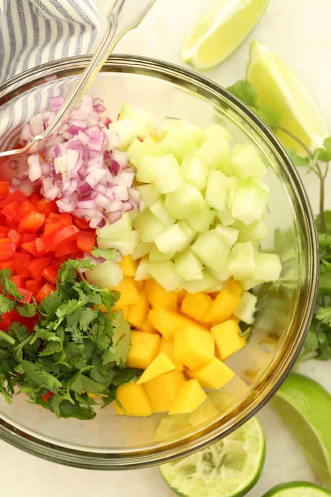 A clear glass mixing bowl filled with chopped fruit and herbs.