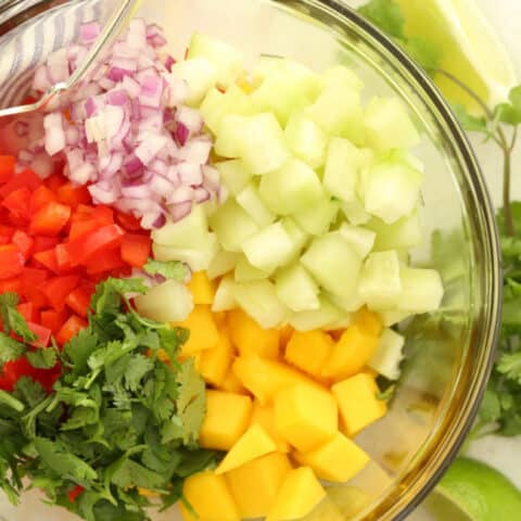 A clear glass mixing bowl filled with Mango Salsa.