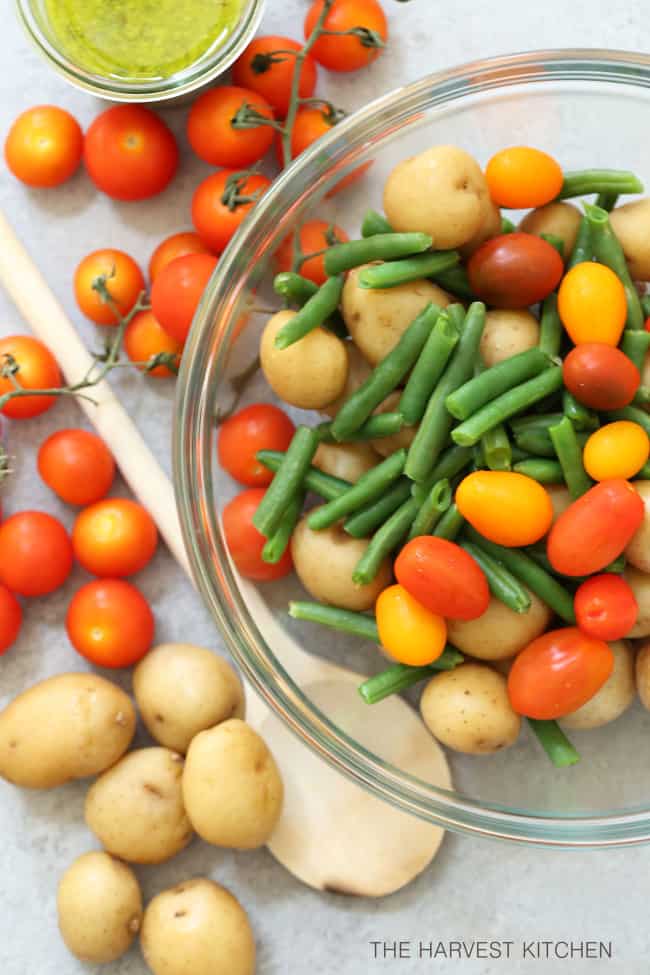 A clear glass mixing bowl filled with green beans and cherry tomatoes.