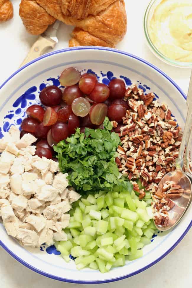 a blue and white bowl filled with chopped cooked chicken< chopped celery, pecans and red grapes