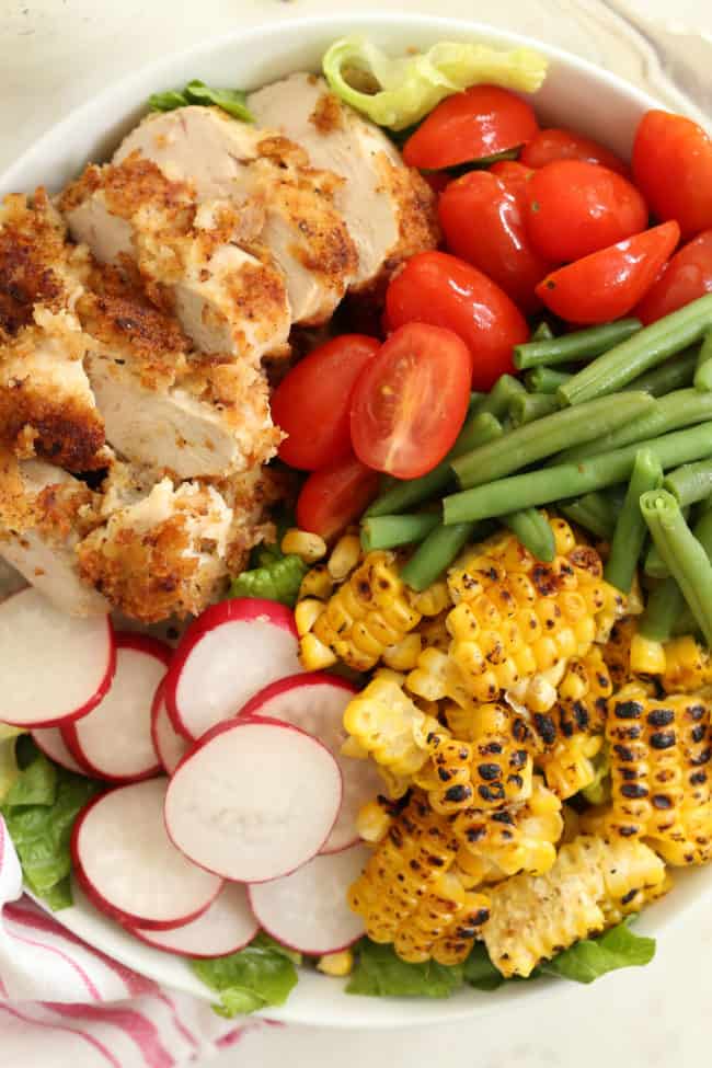 white bowl filled with lettuce, corn, radishes, string beans tomatoes and meat 