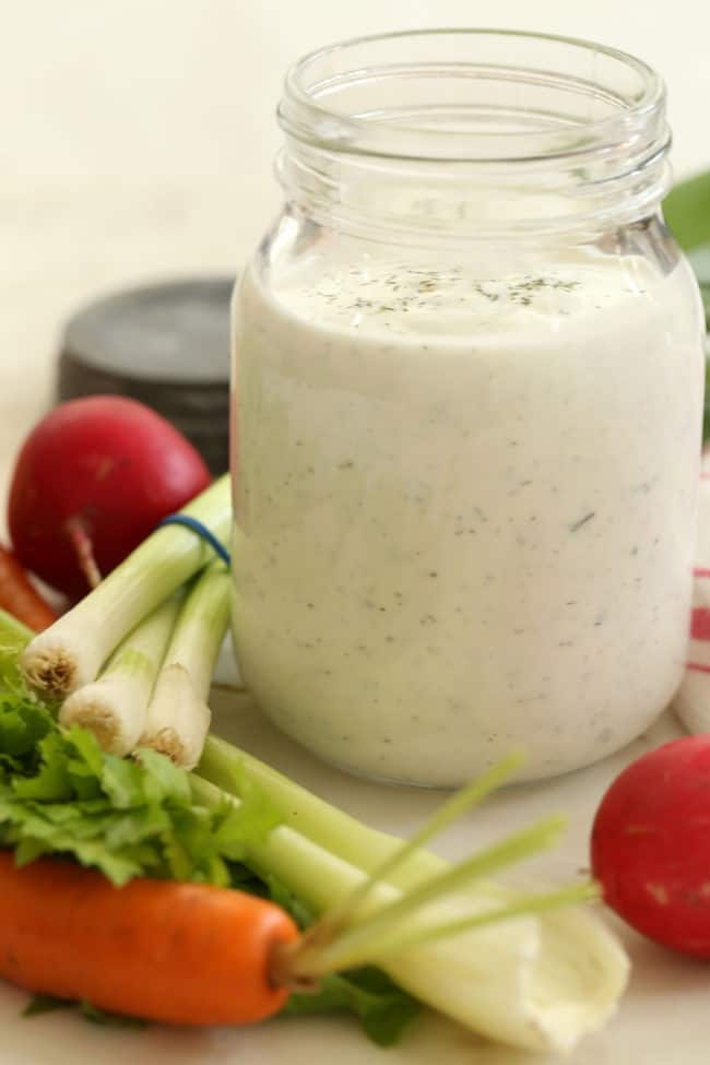 clear glass mason jar filled with ranch dressing. Carrots, celery, green onion and radishes lay next to the jar.