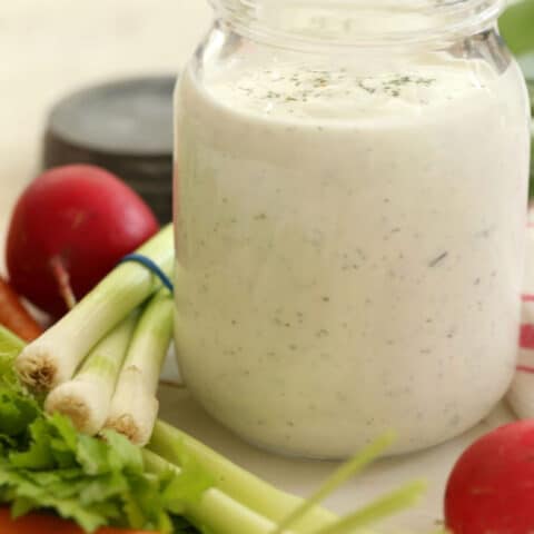 clear glass mason jar filled with ranch dressing. Carrots, celery, green onion and radishes lay next to the jar.
