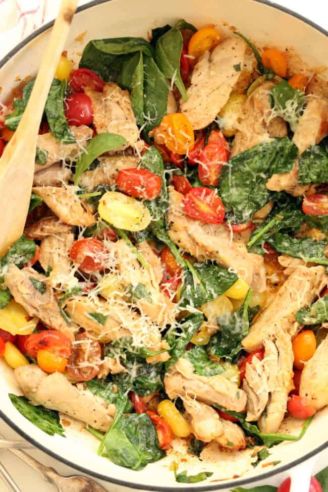 A white skillet filled with cooked chiken, spinach and tomatoes for an easy Italian chicken skillet recipe.