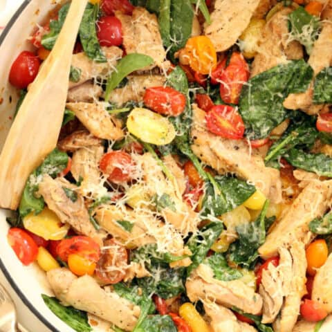 A white skillet filled with cooked chicken, cherry tomatoes and spinach for an Easy Italian Chicken Skillet.