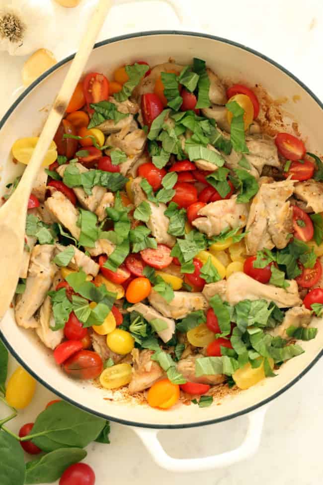A white pan filled with cooked poultry, cherry tomatoes and spinach.
