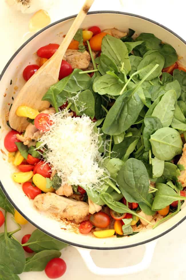 A white skillet filled with cooked chicken, cherry tomatoes and spinach for an easy Italian Chicken Skillet.