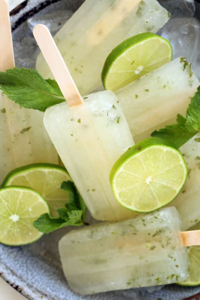 A gray dish filled with lime popsicles garnished with slices of lime and mint leaves.