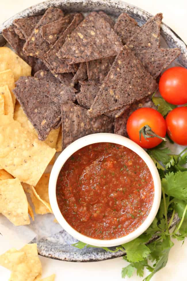 A gray platter filled with tortilla chips. A white bowl filled with red sauce sits next to the chips.