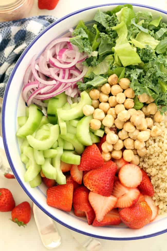 bowl filled with lettuce and kale, cucumbers, red onion, quinoa and berries